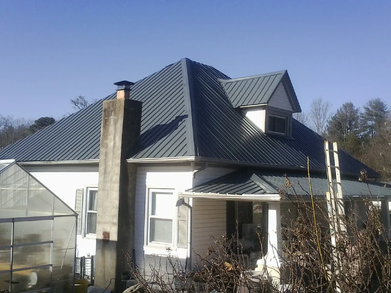 Dark blue standing seam metal roof on a white farmhouse with dormer — Slate & Tile Roof Repair by Roofing Brothers in Elk Grove