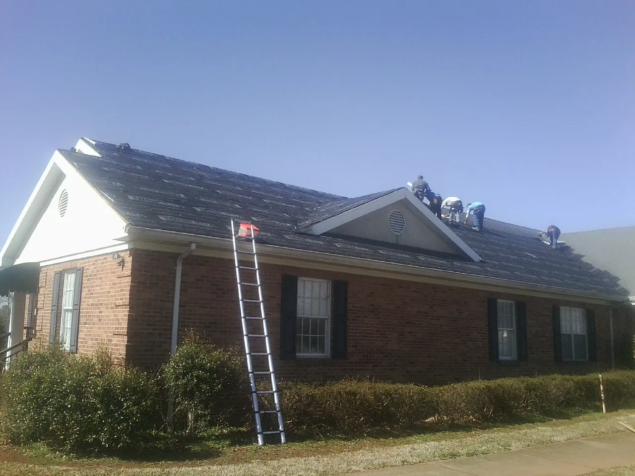 Crew tearing shingles off a brick ranch roof with a ladder set — Metal Roof Repair work by our crew in Elk Grove