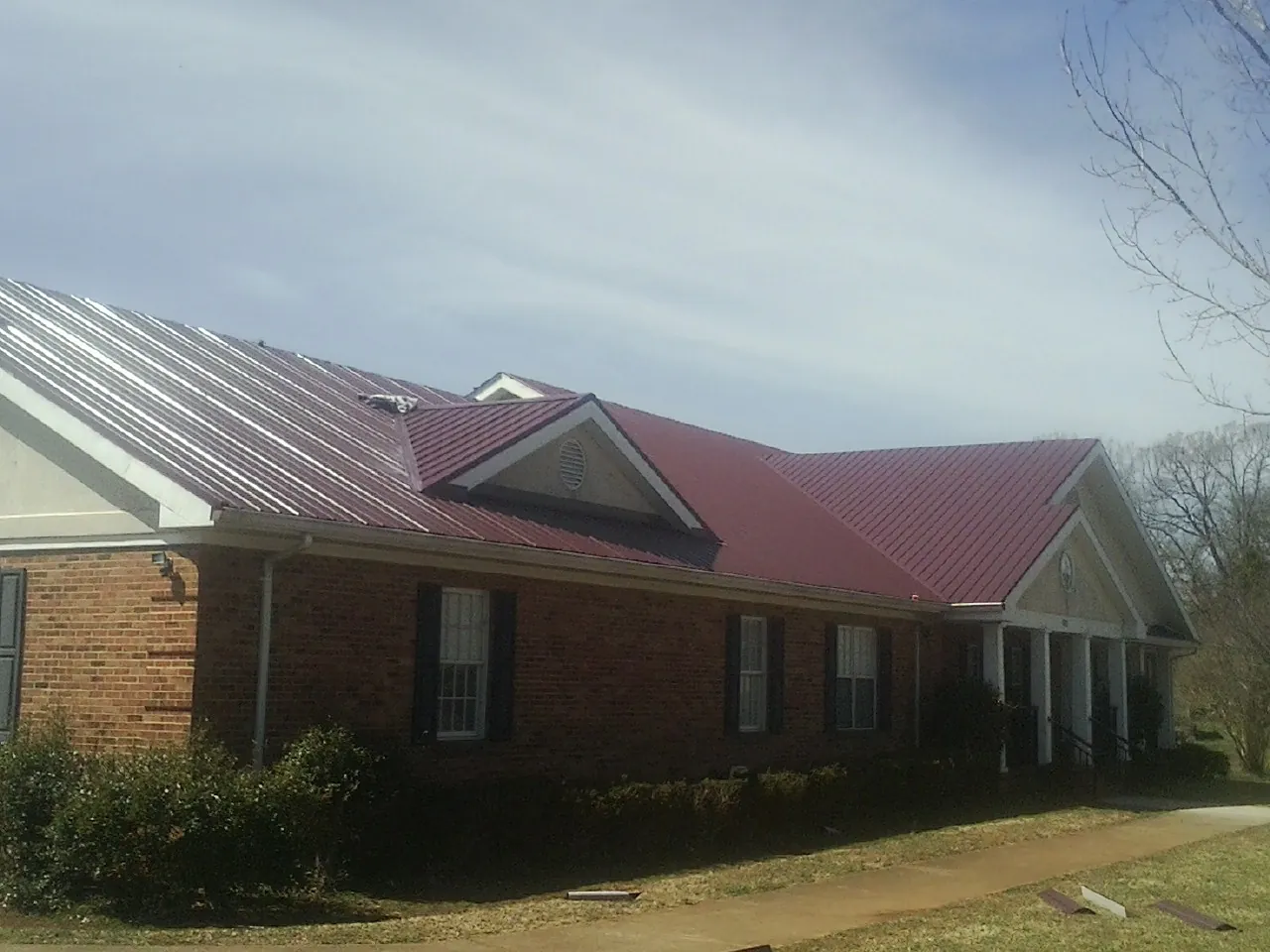 Red metal roof with gabled entries on a long brick building, from a Hail Damage Roof Repair job in Elk Grove