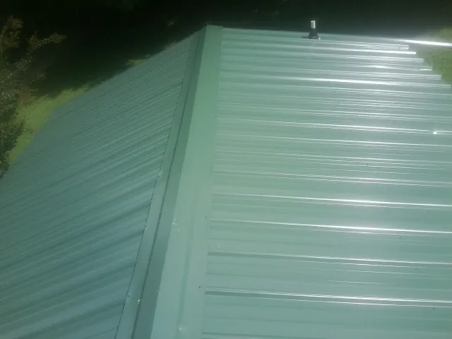 New green metal panels meeting at the ridge of a roof — Flat Roof Repair work by our crew in Elk Grove