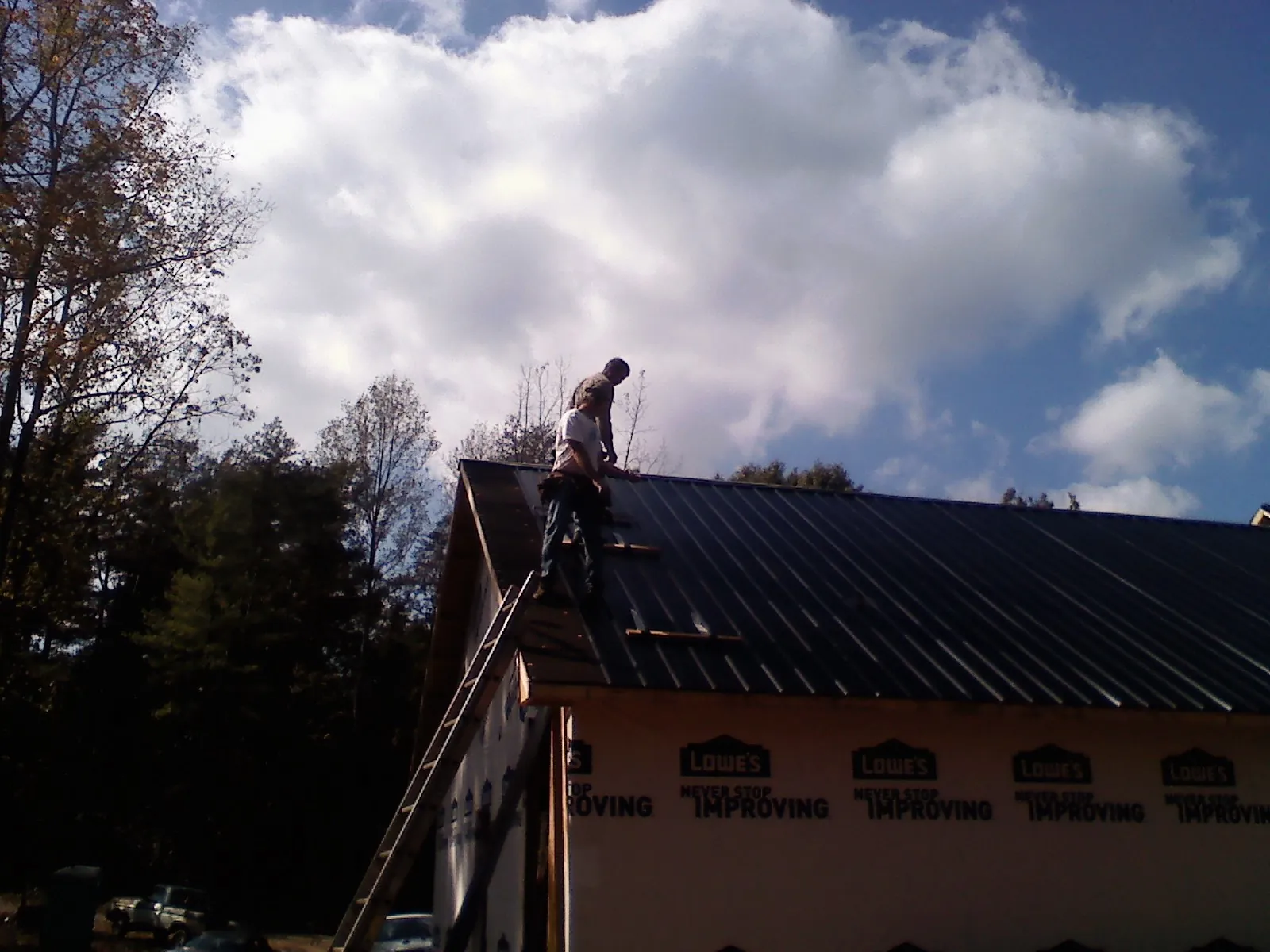 Roofer fastening dark metal panels high against a cloudy sky, from a Roof Inspection job in Elk Grove
