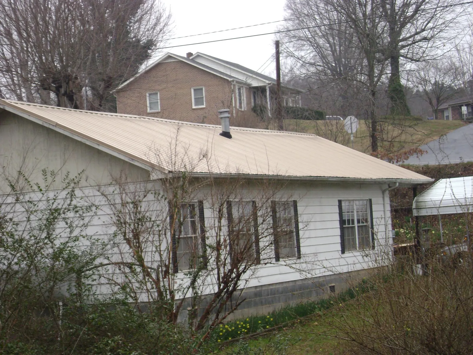 Tan metal roof on a white sided house set into a hillside — Commercial Roofing by Roofing Brothers in Elk Grove